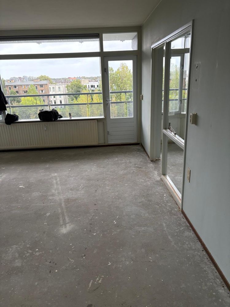 Dezelfde woonkamer in Den Haag na de ontruiming: leeg en laminaat verwijderd tot op de betonvloer