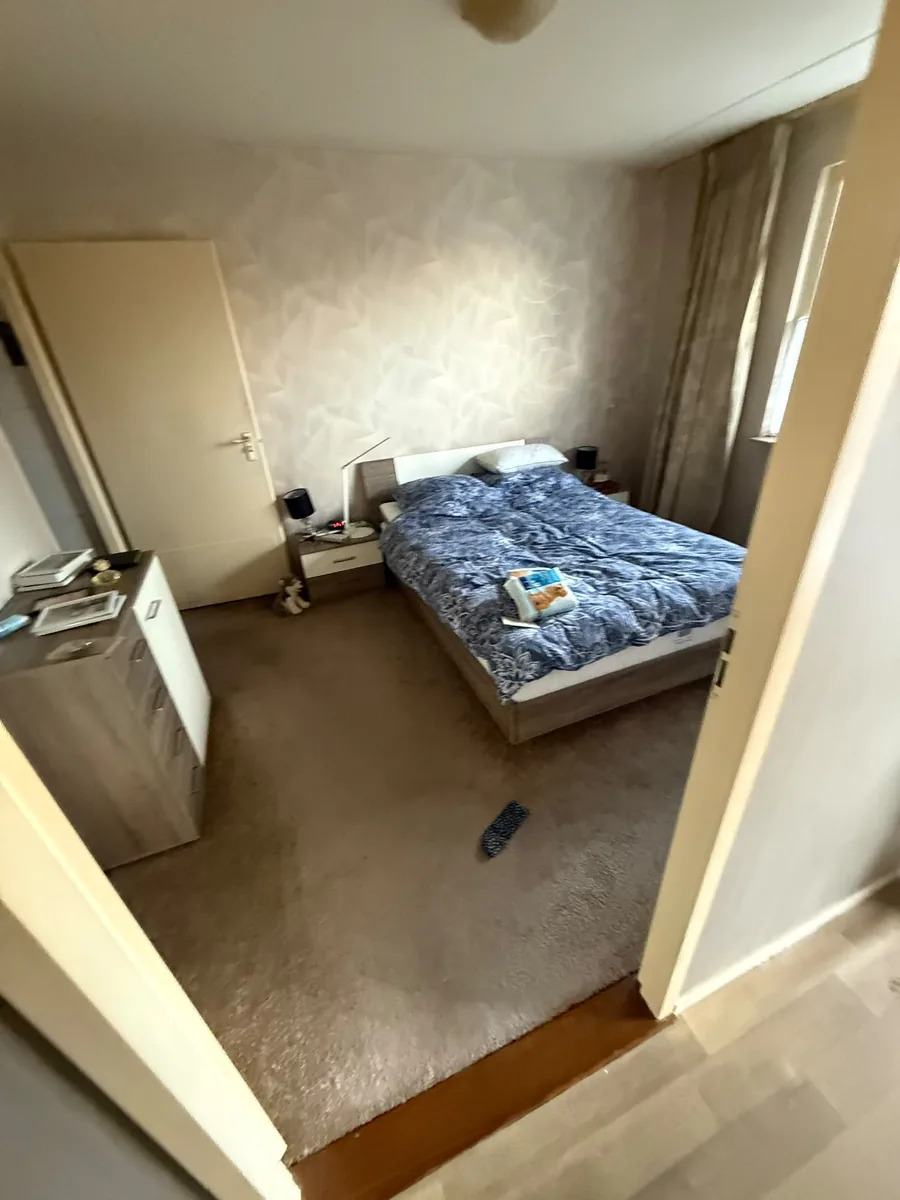 Slaapkamer in Vlaardingen voor de ontruiming, met bed, ladekast en vloerbedekking