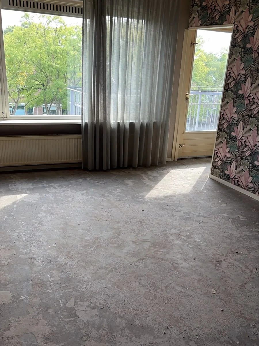 Dezelfde woonkamer in Vlaardingen na de ontruiming: leeg en de vloer verwijderd tot op de ondervloer