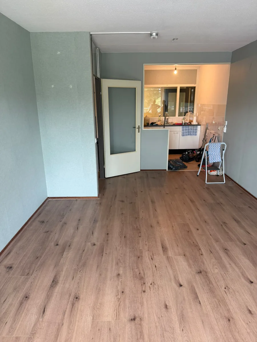 Dezelfde woonkamer in Voorburg na de ontruiming: leeg opgeleverd, met zicht op de keuken
