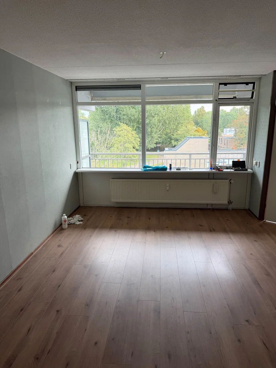 Dezelfde woonkamer in Voorburg na de ontruiming: leeg bij de raampartij en het balkon