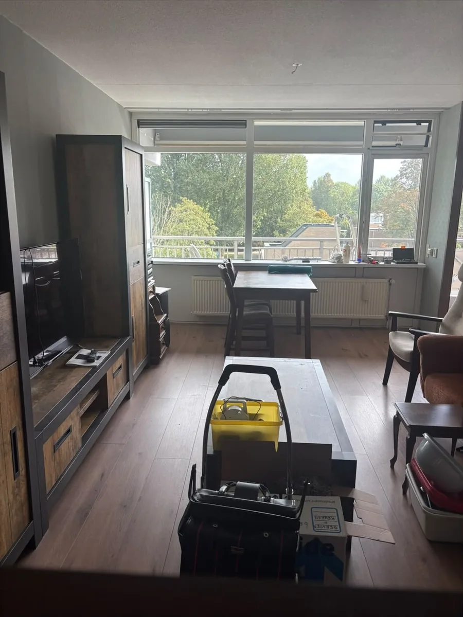 Woonkamer in Voorburg voor de ontruiming, met tv-meubel, eettafel en verhuisdozen